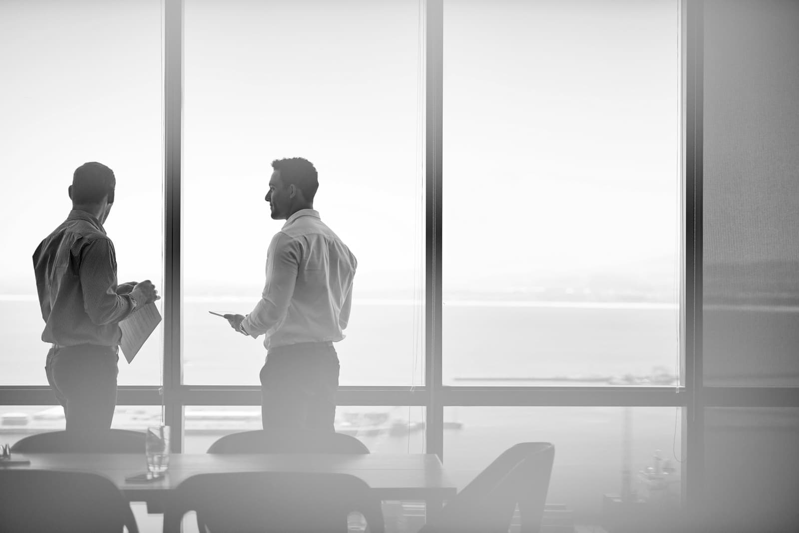 Zwei Führungskräfte im Gespräch am Panoramafenster eines Büroturms